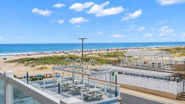 Vista sulla spiaggia dal balcone, con tavoli da picnic e un'area salotto coperta.