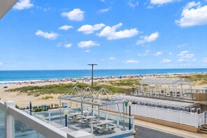 Blick auf den Strand vom Balkon aus, mit Picknicktischen und einer überdachten Sitzgelegenheit.
