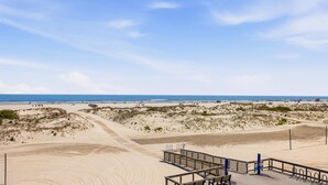 Una spiaggia con una passerella di legno, dune sabbiose e una vista limpida sull'oceano.
