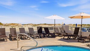 Zona piscina con sedie a sdraio e ombrelloni, vista libera sulla spiaggia e piscina.