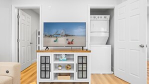 Een woonkamer met een televisie op een houten dressoir, een witte kast met glazen deuren en een witte wasmachine.