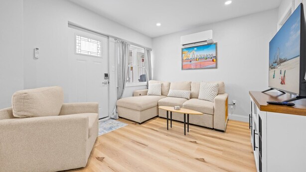 Een moderne woonkamer met een beige modulaire bank, een fauteuil, een bijzettafeltje en een flatscreen televisie op een houten kast.