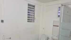 Een kleine, schone badkamer met toilet, wastafel en een raam met luxaflex.