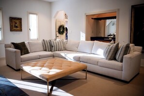 A living room with a sectional sofa, a tufted ottoman, and a large mirror.