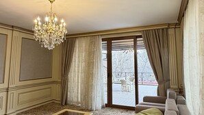 A spacious living room with a large sectional sofa, a glass-top coffee table, a chandelier, and a view through a sliding glass door to an outdoor patio. - Sky Town Mountain Resort (Chorvoq)