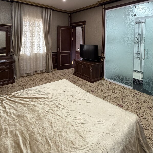 A bedroom with a bed, a television on a wooden cabinet, a wardrobe, and a bathroom with a glass door. - Sky Town Mountain Resort (Chorvoq)