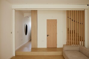 Ein modernes Interieur mit Holzboden, einem beigefarbenen Sofa, einer Holztür und einer Treppe mit hölzernen Geländern.