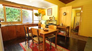 A dining area with a wooden table, chairs, a vase with flowers, and a window with a view of greenery.