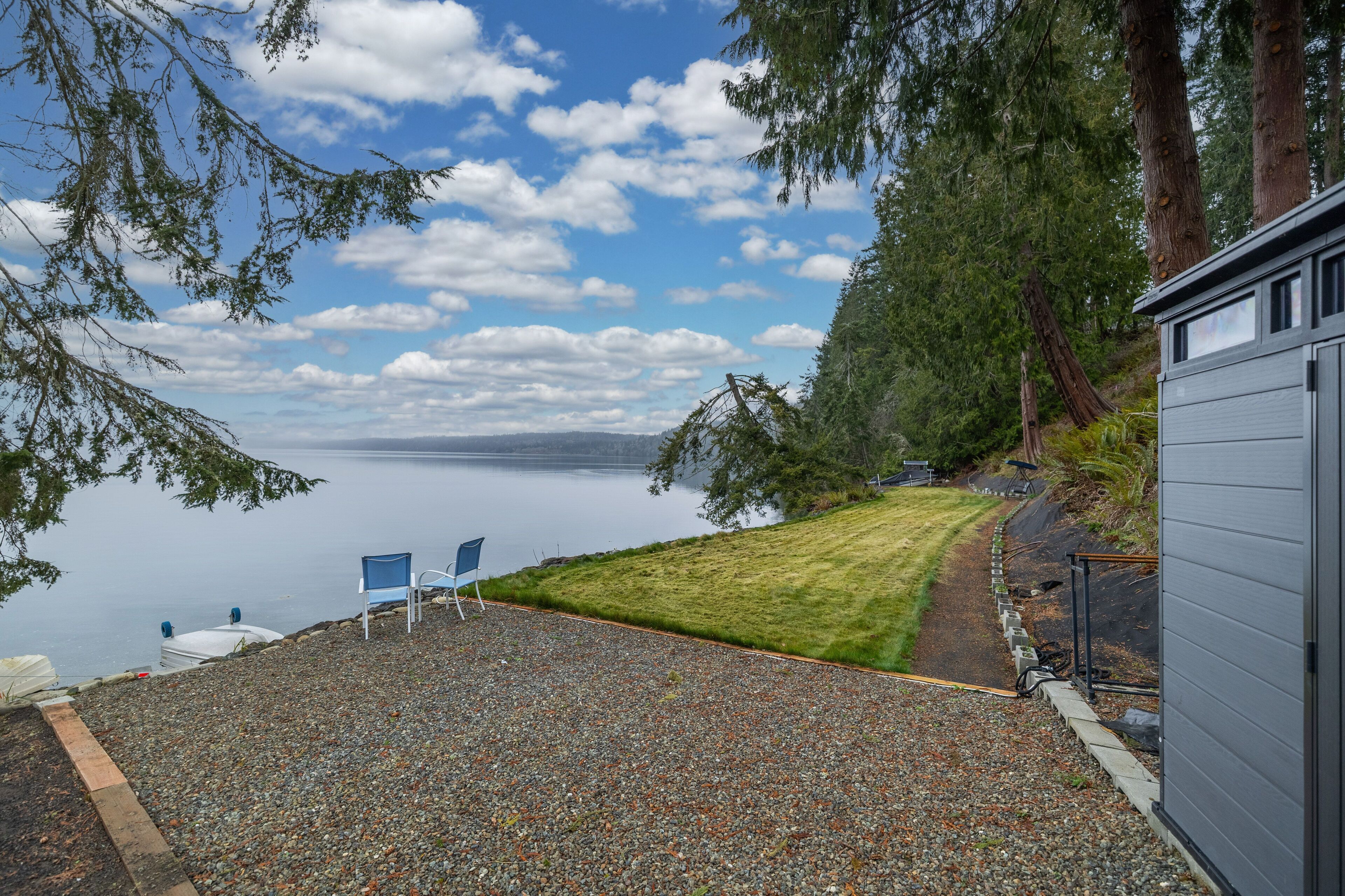 Une terrasse en gravier avec une chaise bleue, une pelouse et une vue sur un lac.
