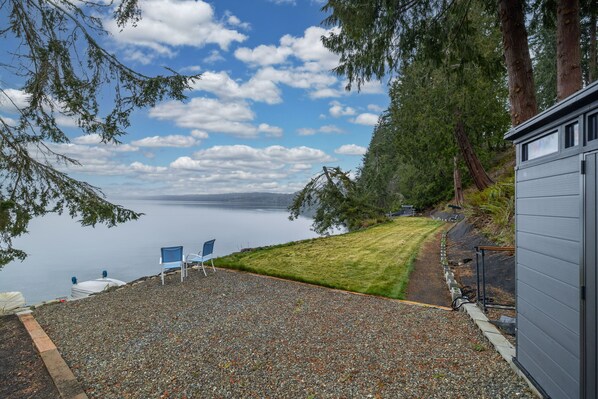 Un patio de grava con una silla azul, una zona verde y vistas a un lago.