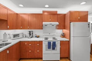 A modern kitchen with wooden cabinets, a white stove, a microwave, and a refrigerator.