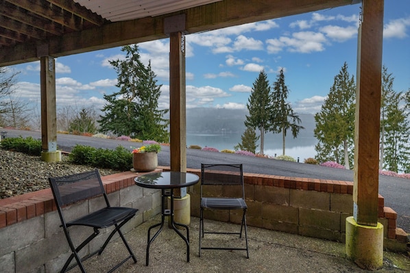 A covered patio with two chairs and a table, overlooking a lake and trees.