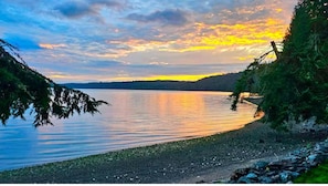 A calm lake at sunset with a clear sky, surrounded by greenery and a wooden fence.