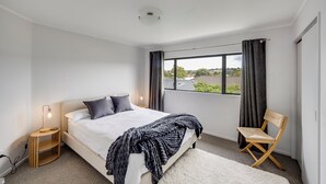 Ein Schlafzimmer mit Bett, Nachttischlampe, Stuhl und einem Fenster mit Vorhängen.