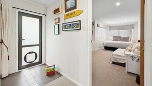 Habitació d'hotel amb un llit, una petita taula de nit, una finestra amb cortines, una porta amb ull de brau i un passadís amb una porta que condueix a una altra habitació.