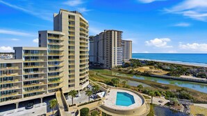 Un hotel moderno de gran altura con varios balcones, piscina y vista a la playa y al océano.