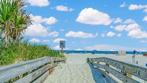 Una pasarela de madera que lleva a una playa con palmeras y cielo despejado.