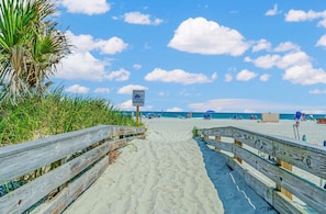 A wooden boardwalk leading to a beach with palm trees and a clear sky. - 🌊Stunning Oceanfront | Pool | Ocean Creek South CC-8🌊 (Myrtle Beach)
