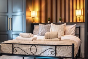 Un lit bien fait, avec des oreillers et une couverture, une lampe de chevet et un luminaire fixé au mur.