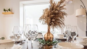 A dining table set with white plates, bowls, and clear wine glasses, centered by a vase with dried pampas grass. - Open Mind Property- 6BR Home, Hot Tub & Free Parking (Fareham , PO15 5RS)