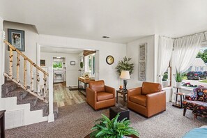 A living room with a staircase, two brown leather chairs, a small table, a lamp, and a view of the outside. - Cozy Downtown Cottage Near Beach and Pier (East Tawas)