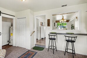 A kitchen with a bar area, two bar stools, a large mirror, and a view of the outdoors. - Cozy Downtown Cottage Near Beach and Pier (East Tawas)