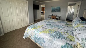 Een slaapkamer met een groot bed, een bureau, een stoel en een deur.