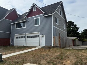 Une maison à deux étages, avec une façade grise, deux portes de garage et un toit rouge.