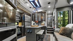 A compact kitchen with a central island, built-in appliances, and a large window providing a view of the outdoors. - The "Waldorf Astoria of RVs" A Five-Star Forest Escape (Clallam County)