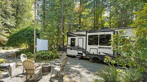 A recreational vehicle (RV) parked in a forested area with outdoor seating and a white canopy. - The "Waldorf Astoria of RVs" A Five-Star Forest Escape (Clallam County)