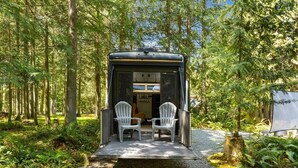 A small, enclosed RV with two chairs outside, surrounded by a forest. - The "Waldorf Astoria of RVs" A Five-Star Forest Escape (Clallam County)