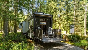 A mobile home with a deck, two chairs, and a gravel path surrounded by trees. - The "Waldorf Astoria of RVs" A Five-Star Forest Escape (Clallam County)