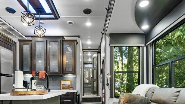 A compact RV interior with a kitchenette, a seating area, and a window providing a view of greenery. - The "Waldorf Astoria of RVs" A Five-Star Forest Escape (Clallam County)