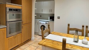 Una cocina compacta con armarios de madera, horno empotrado, lavadora y mesa de comedor con sillas.