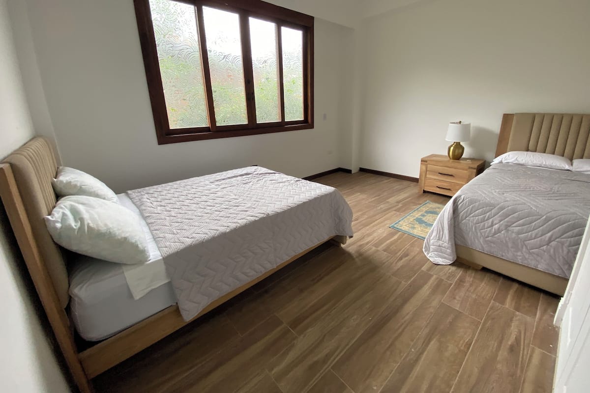Une chambre avec deux lits, un plancher en bois, une fenêtre avec du verre dépoli et une table de chevet avec une lampe.