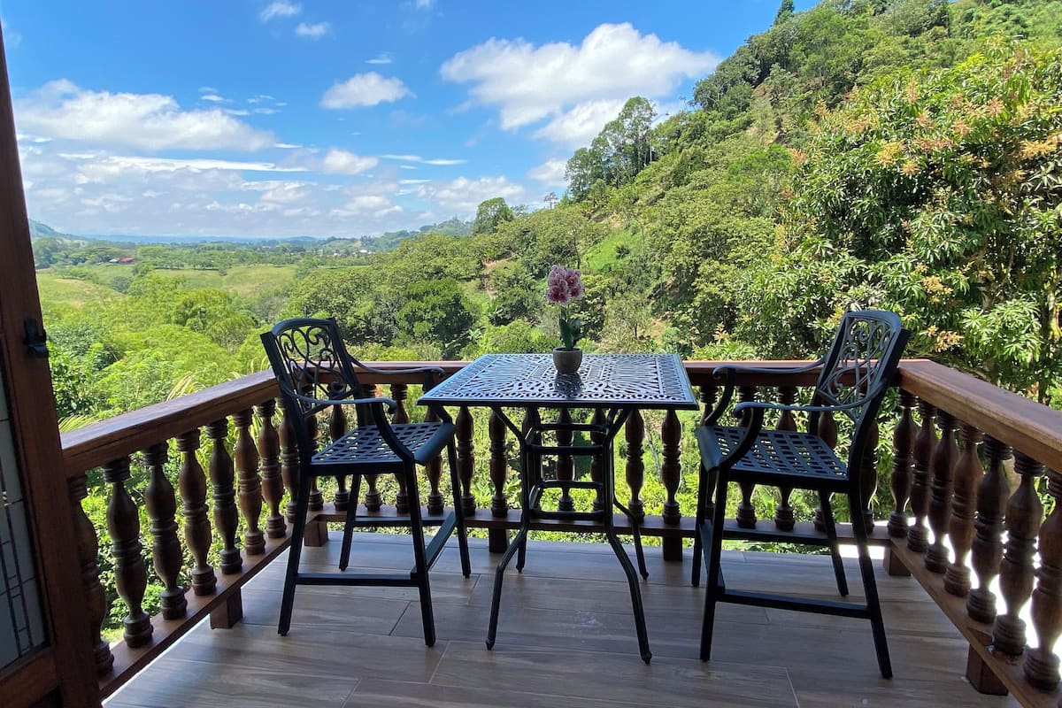 Un balcon avec une table et des chaises, donnant sur un paysage verdoyant et luxuriant.