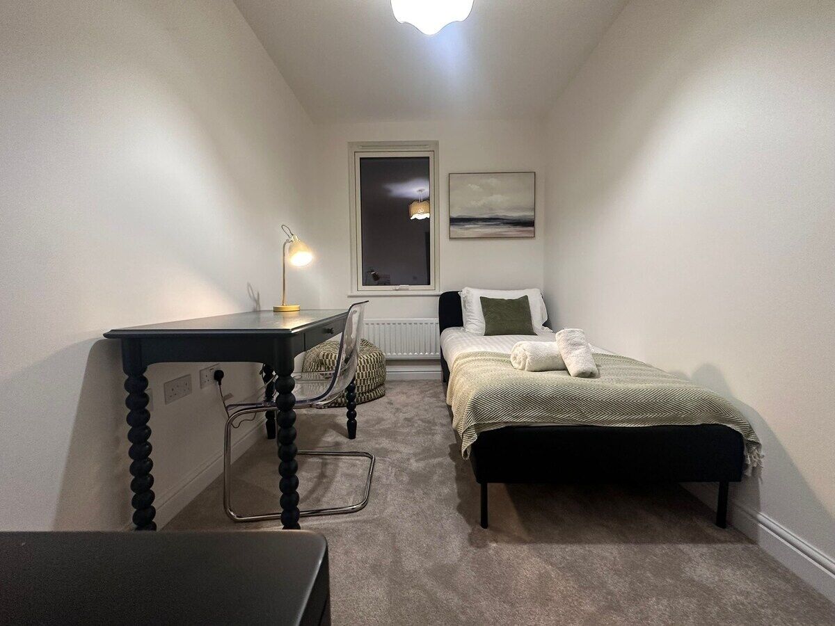 Um quarto pequeno e aconchegante, com uma cama, uma escrivaninha e uma cadeira.