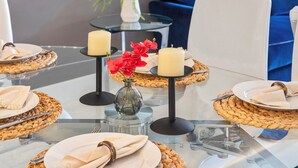 Una mesa de comedor con platos, servilletas y velas, ubicada en una habitación moderna con una silla azul y un jarrón pequeño con flores rojas.