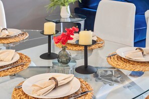 Ein Esstisch mit Tellern, Servietten und Kerzen, in einem modernen Raum mit blauem Stuhl und einer kleinen Vase mit roten Blumen.