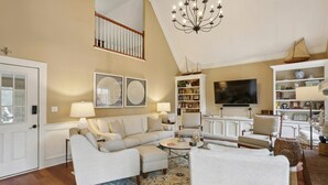 A spacious living room with a high ceiling, a chandelier, a large flat-screen TV, and a bookshelf filled with books and decorative items. - Quiet retreat in Peachtree Corners (Norcross)