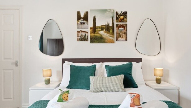 Ein Hotelzimmer mit einem Bett, zwei Nachttischen, einem Spiegel und Wandbildern.