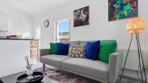 Ein modernes Wohnzimmer mit grauem Sofa, farbenfrohen Kissen, einem schwarzen Couchtisch und einer Stehlampe.