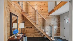 Eine Holztreppe mit Geländer, ein Konsolentisch mit Lampe und Vase sowie eine Tür mit Fenster.