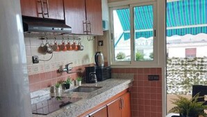 Een kleine keuken met houten kastjes, een granieten aanrechtblad en een raam met uitzicht op een gebouw.