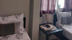Een hotelkamer met een bed, nachtkastje met een lamp, raam met gordijnen en een airconditioner aan de muur.