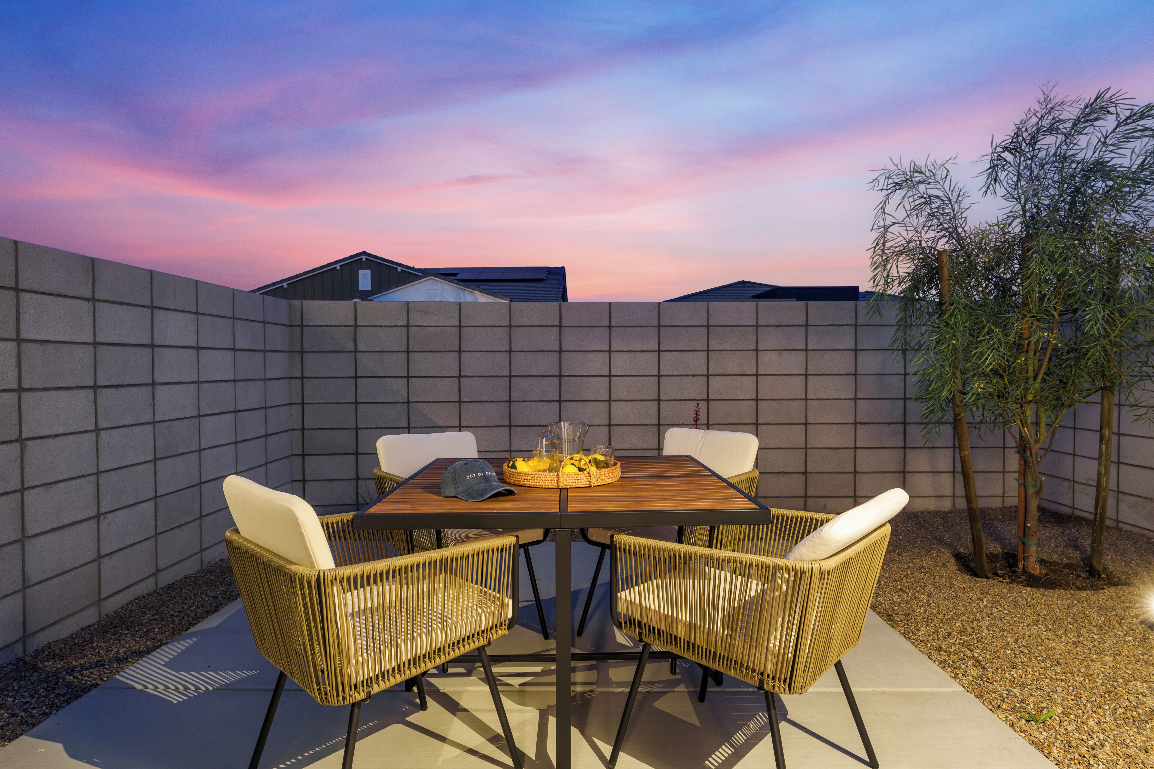 A rectangular outdoor dining area with a wooden table and wicker chairs, surrounded by a low concrete wall.