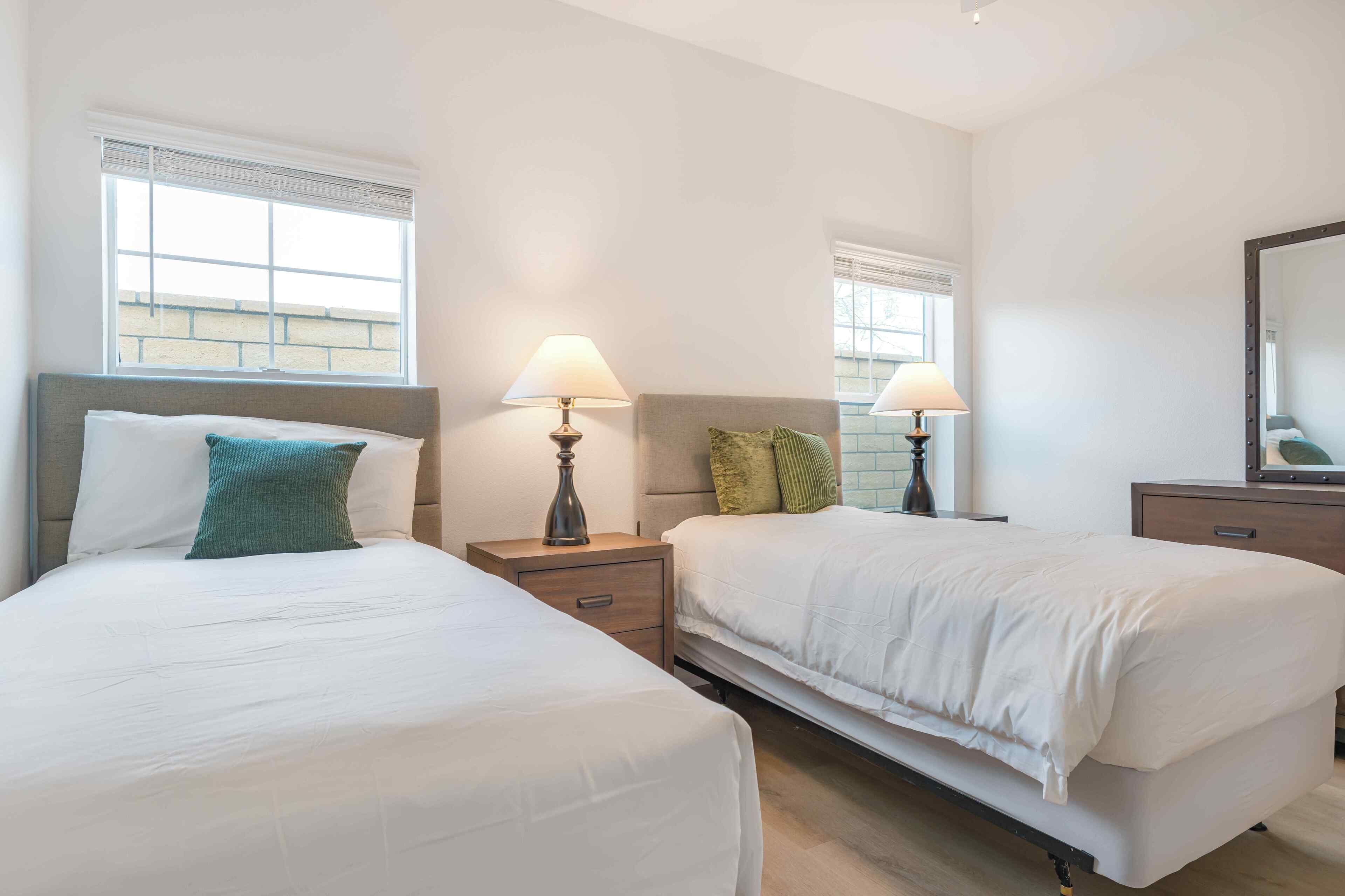 Une chambre d’hôtel avec deux lits, des lampes de chevet, un miroir et une fenêtre.