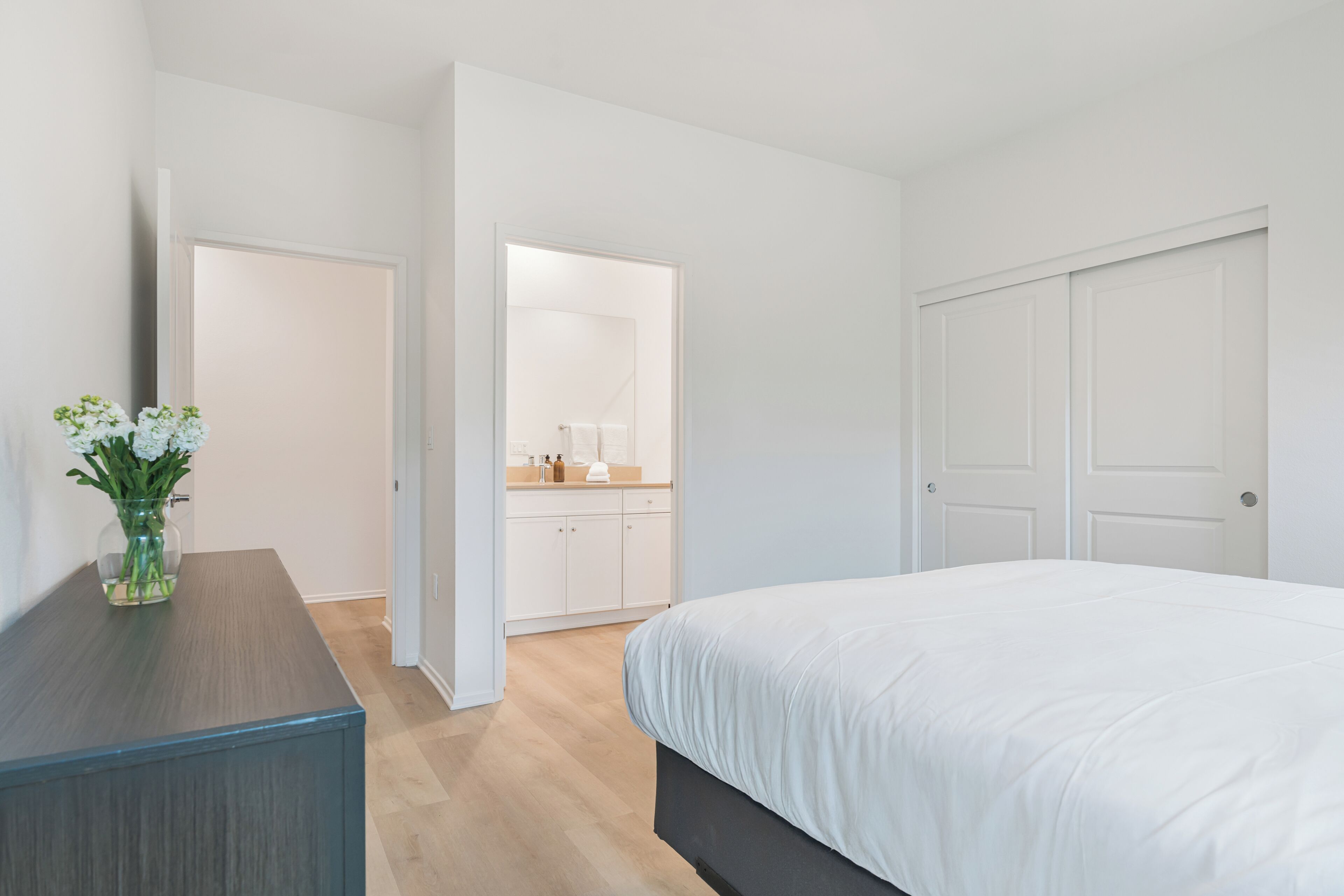 A bedroom with a bed, a dresser, a mirror, and a door leading to a bathroom.