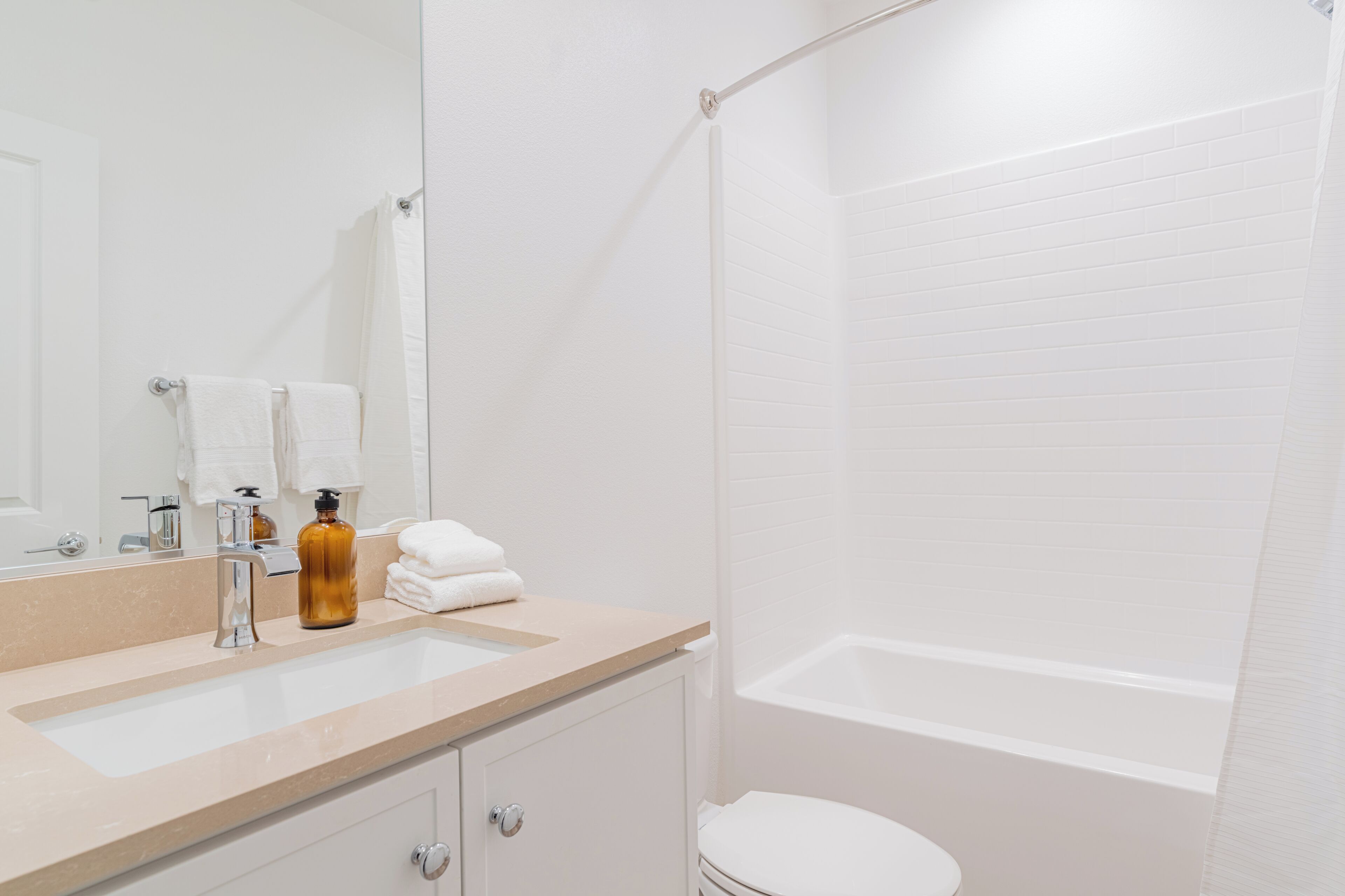 A bathroom with a sink, mirror, toiletries, and a bathtub.