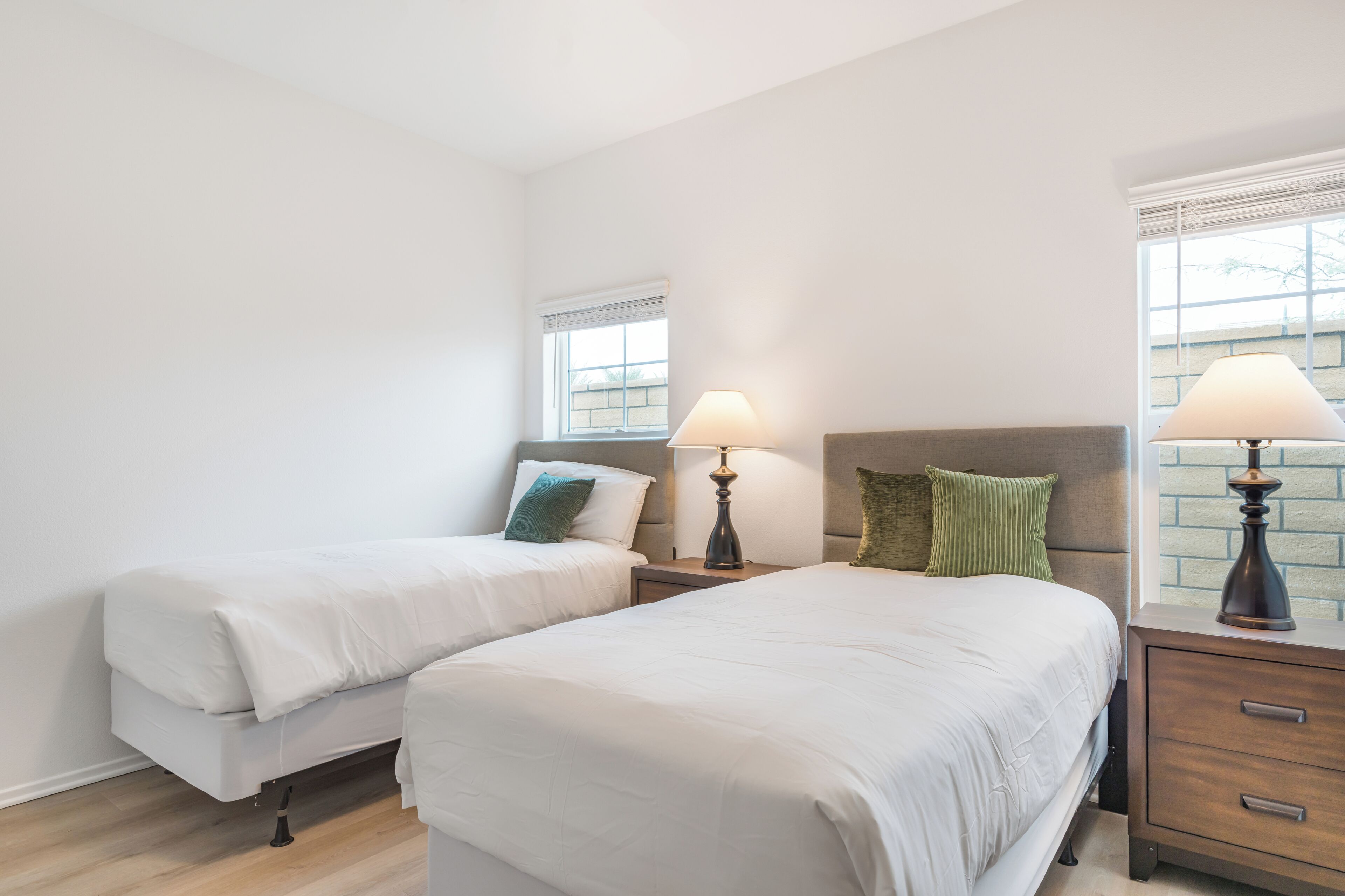 A bedroom with two beds, nightstands, lamps, and a window.